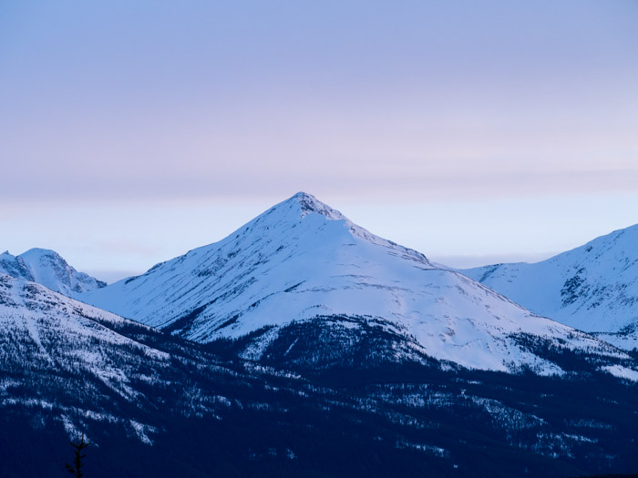 Snow covered sharp mountain peak with sunset hues.