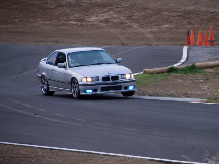 BMW E36 hopping a berm at Thunderhill, one wheel in air.