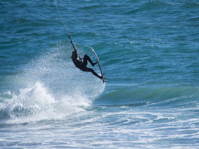Wind surfer jumps feet above the surf with a water plume.